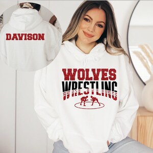 May include: White hoodie with red glitter text that says "WOLVES WRESTLING" and a graphic of two wrestlers in a circle. The back of the hoodie has red glitter text that says "DAVISON".