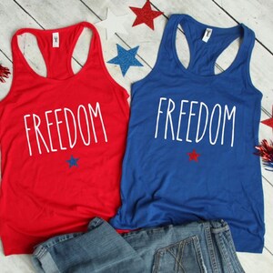 Puede incluir: Dos camisetas sin mangas con la palabra "FREEDOM" impresa en ellas. Una camiseta sin mangas es roja y la otra es azul. Ambas camisetas sin mangas tienen una peque&ntilde;a estrella roja impresa debajo de la palabra "FREEDOM".