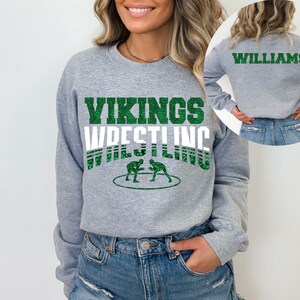 May include: Gray sweatshirt with green glitter text that says "Vikings Wrestling" and a graphic of two wrestlers. The back of the sweatshirt has the text "Williams" in green glitter.