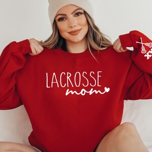 May include: Red sweatshirt with the text "LACROSSE mom" and a small heart in white. The right sleeve has the text "JAX" and a white lacrosse stick graphic.