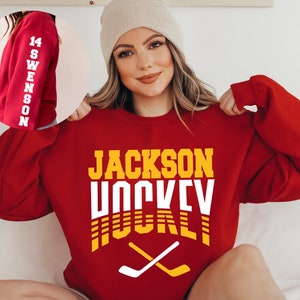 May include: Red sweatshirt with the text "JACKSON HOCKEY" in yellow and white letters. The sweatshirt has a white hockey stick graphic with yellow accents.