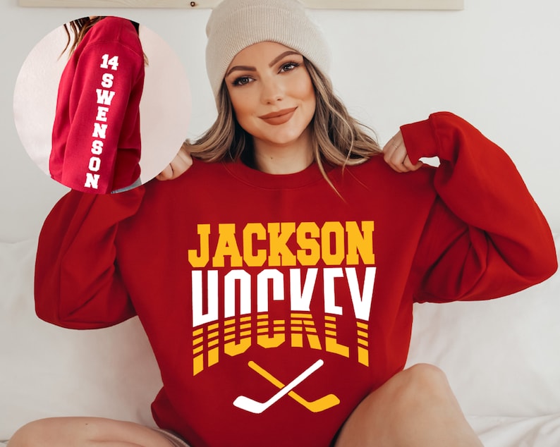 May include: Red sweatshirt with the text "JACKSON HOCKEY" in yellow and white letters. The sweatshirt has a white hockey stick graphic with yellow accents.
