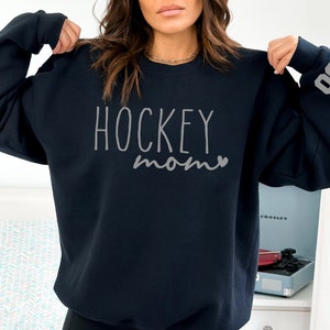 May include: A navy blue sweatshirt with the text "HOCKEY mom" in gray lettering and a small heart. The number "09" is on the sleeve.