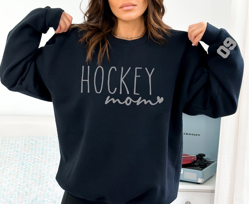 May include: A navy blue sweatshirt with the text "HOCKEY mom" in gray lettering and a small heart. The number "09" is on the sleeve.