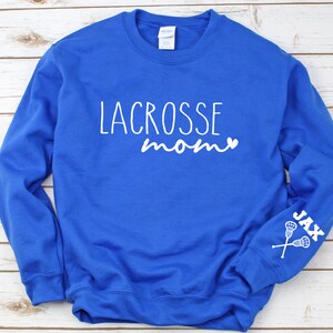May include: Royal blue sweatshirt with white text that reads "Lacrosse mom" with a heart symbol. The left sleeve has white text that reads "Jax" with a lacrosse stick graphic.