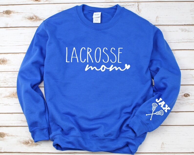 May include: Royal blue sweatshirt with white text that reads "Lacrosse mom" with a heart symbol. The left sleeve has white text that reads "Jax" with a lacrosse stick graphic.