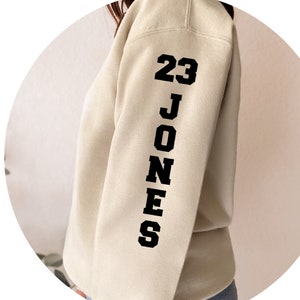 May include: A cream colored sweatshirt with black text on the sleeve that reads "23 JONES".