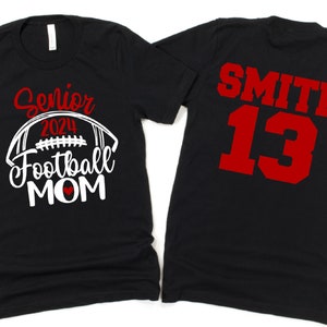 Op de afbeelding: Twee zwarte T-shirts. E&eacute;n shirt zegt "Senior 2024 Football Mom" met een witte voetbal en een rood hart. Het andere shirt heeft "SMITH 13" in rood op de achterkant.