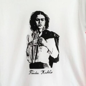May include: White t-shirt with a black and white image of Frida Kahlo and the text "Frida Kahlo" printed on the front.