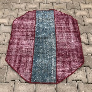 Könnte beinhalten: Achteckiger Teppich mit einem zentralen blauen Feld, das von weinroten Feldern flankiert wird. Der Teppich hat ein abgenutztes, Vintage-Aussehen mit verblassten Farben und sichtbaren Gebrauchsspuren. Die Kanten sind mit einem dunkleren weinroten Rand versehen.