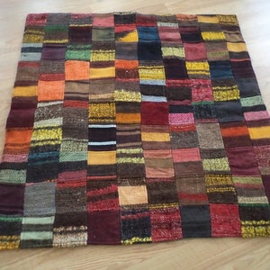 May include: A patchwork quilt with a variety of textured fabrics in a grid pattern. The quilt features squares of various colors, including brown, orange, yellow, and burgundy. The quilt is likely made of wool or a similar material.