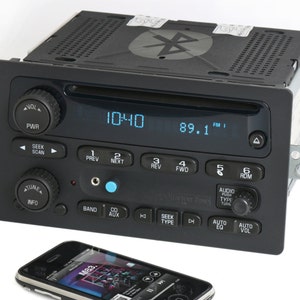 May include: A black car stereo with a digital display showing 10:40 and 89.1 FM. The stereo has buttons for power, seek, scan, tune, info, prev, next, rev, fwd, 5, 6, band, cd, aux, seek, type, auto eq, auto vol, and audio push type turn. A smartphone is in the foreground.