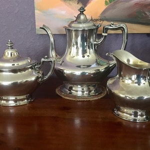 May include: A silver tea set with a teapot, creamer, and sugar bowl. The set is polished and shiny, reflecting the light.