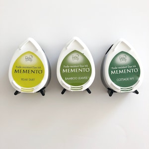 May include: Three ink pads in a teardrop shape with white lids and black bases. The ink pads are labeled "Dew Drop Fade-resistant Dye Ink Memento" with the colors Pear Tart, Bamboo Leaves, and Cottage Ivy.