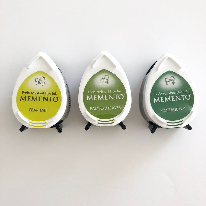 May include: Three ink pads in a teardrop shape with white lids and black bases. The ink pads are labeled "Dew Drop Fade-resistant Dye Ink Memento" with the colors Pear Tart, Bamboo Leaves, and Cottage Ivy.