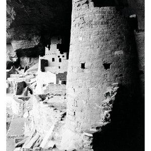 Puede incluir: Una fotograf&iacute;a en blanco y negro de una vivienda en un acantilado en una cueva. La vivienda est&aacute; hecha de piedra y tiene una torre en el lado derecho de la imagen. La torre es redonda y tiene una peque&ntilde;a ventana en el lado.