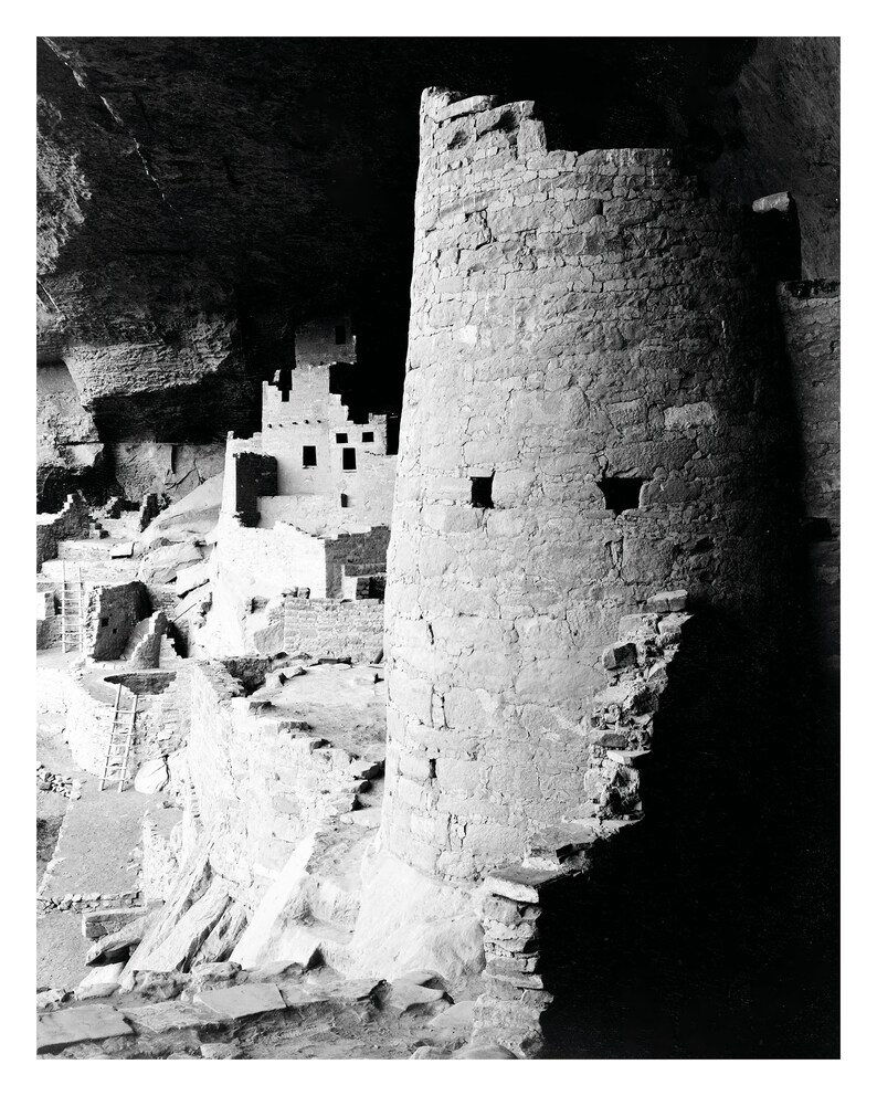 Puede incluir: Una fotograf&iacute;a en blanco y negro de una vivienda en un acantilado en una cueva. La vivienda est&aacute; hecha de piedra y tiene una torre en el lado derecho de la imagen. La torre es redonda y tiene una peque&ntilde;a ventana en el lado.
