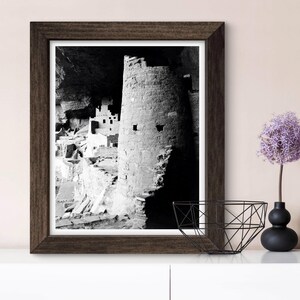 Puede incluir: Fotograf&iacute;a en blanco y negro de una vivienda en un acantilado en un ca&ntilde;&oacute;n. La vivienda est&aacute; hecha de piedra y tiene una torre redonda. La fotograf&iacute;a est&aacute; enmarcada en un marco de madera oscura.