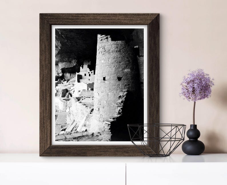 Puede incluir: Fotograf&iacute;a en blanco y negro de una vivienda en un acantilado en un ca&ntilde;&oacute;n. La vivienda est&aacute; hecha de piedra y tiene una torre redonda. La fotograf&iacute;a est&aacute; enmarcada en un marco de madera oscura.