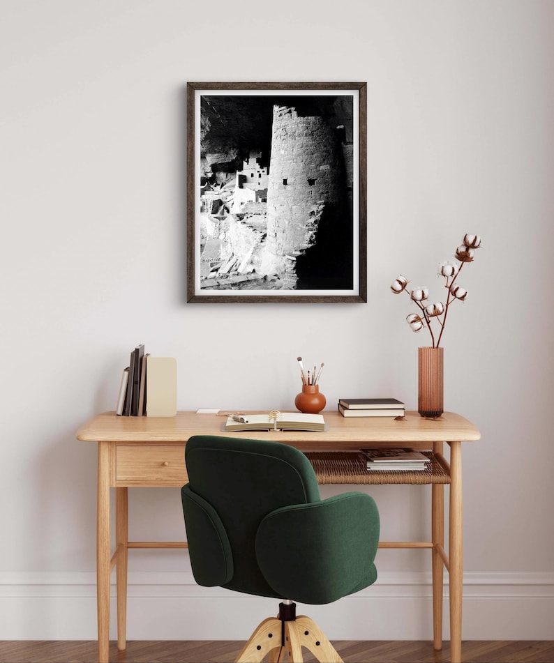 Puede incluir: Fotograf&iacute;a en blanco y negro de una vivienda en un acantilado en una cueva. La foto est&aacute; enmarcada en un marco de madera oscura y est&aacute; colgada en una pared blanca sobre un escritorio de madera con una silla verde.