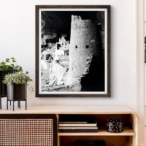 Puede incluir: Fotograf&iacute;a en blanco y negro de una vivienda en un acantilado en una cueva. La vivienda est&aacute; hecha de piedra y tiene una torre redonda. La fotograf&iacute;a est&aacute; enmarcada en un marco de madera oscura.