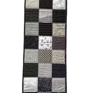 May include: A black and white patchwork table runner with a variety of geometric and floral patterns. The runner is made of fabric squares sewn together.