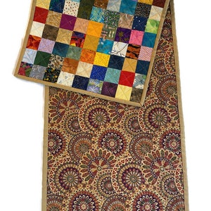 May include: A colourful patchwork quilt table runner with a brown and gold paisley pattern on the reverse side. The runner has a tan border.