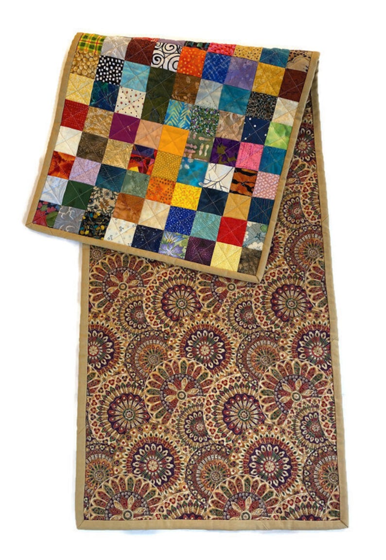 May include: A colourful patchwork quilt table runner with a brown and gold paisley pattern on the reverse side. The runner has a tan border.
