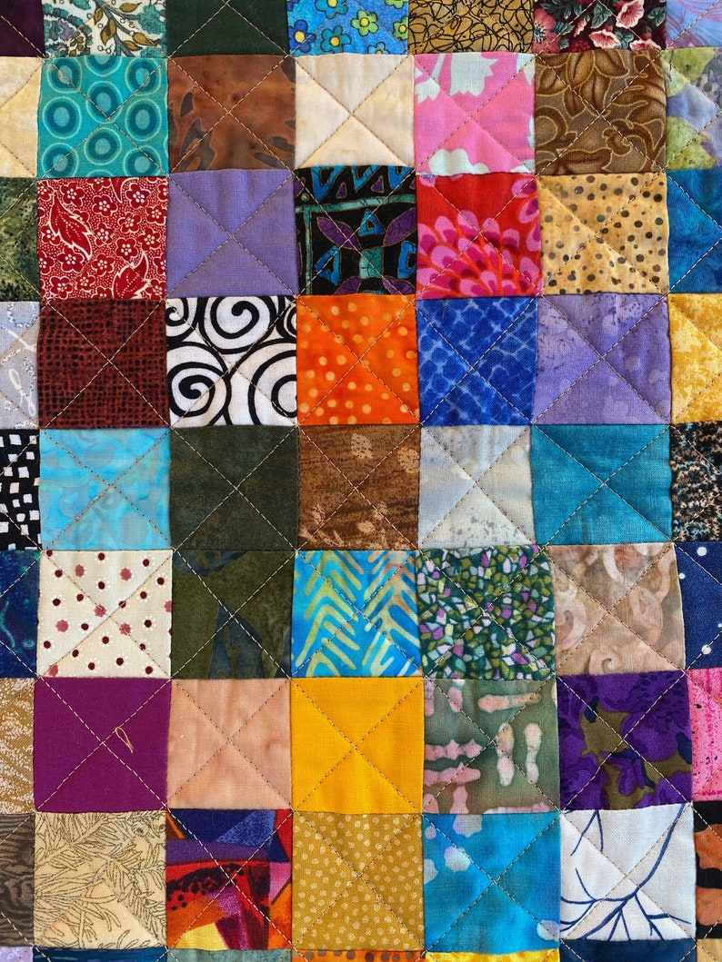 May include: A colourful quilt made of many different fabric squares, each with a unique pattern. The quilt is sewn together in a grid pattern, with each square being a different colour and design. The quilt is a beautiful example of patchwork quilting.