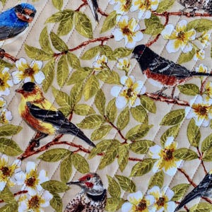 May include: A beige quilted fabric with a floral pattern featuring white flowers and green leaves.  The fabric is decorated with various colorful birds, including a bluebird, a yellow bird, a red-breasted bird, and a brown and white bird.