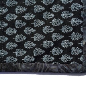 May include: Close-up of a black fabric with a white fern pattern. The fabric has a dark gray border with a subtle swirl pattern.