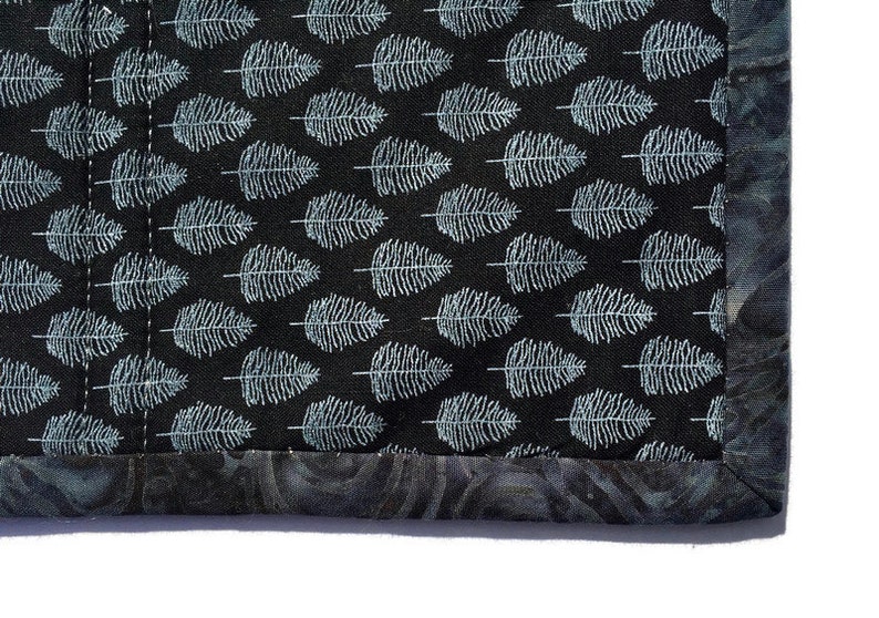 May include: Close-up of a black fabric with a white fern pattern. The fabric has a dark gray border with a subtle swirl pattern.