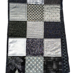 May include: A black and white patchwork quilt with a variety of geometric and floral patterns. The quilt is made of different fabrics and textures, creating a unique and interesting design.