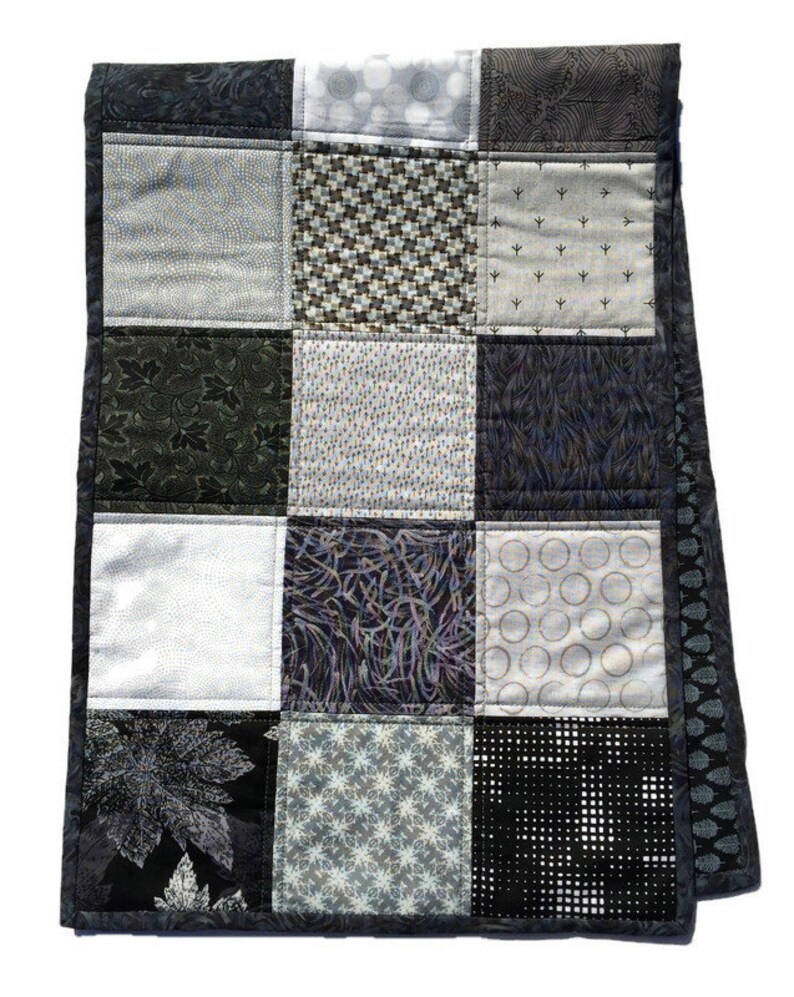 May include: A black and white patchwork quilt with a variety of geometric and floral patterns. The quilt is made of different fabrics and textures, creating a unique and interesting design.