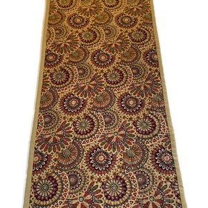 May include: A beige table runner with a repeating pattern of colourful, intricate circles. The circles are in shades of red, green, and purple.