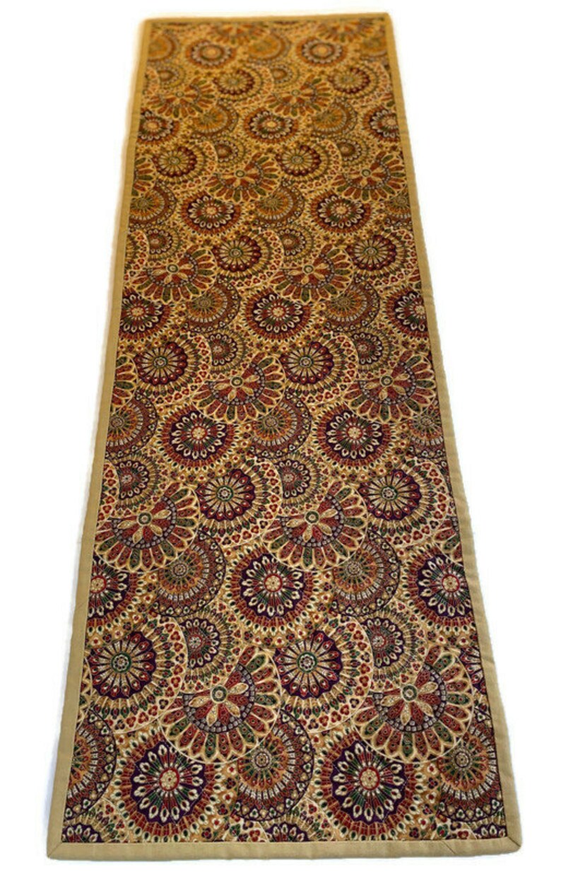 May include: A beige table runner with a repeating pattern of colourful, intricate circles. The circles are in shades of red, green, and purple.