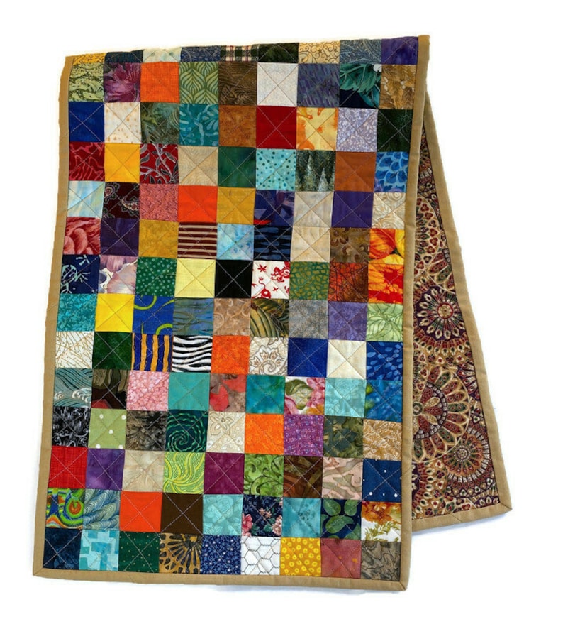May include: A colourful patchwork table runner with a tan border. The runner is made of many different fabrics, each with a unique pattern. The runner is approximately 35 cm wide and 183 cm long.