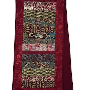 May include: A red quilted table runner with a patchwork design featuring various fabrics in shades of green, brown, and red. The runner is made from repurposed ties and has a floral pattern.