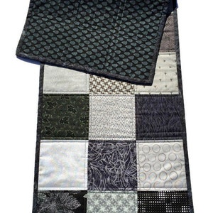 May include: A black and white patchwork table runner with a geometric pattern. The runner is made of different fabrics with various patterns, including leaves, circles, and stars.