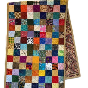 May include: A colourful patchwork table runner with a tan border. The runner is made of many different fabrics, each with a unique pattern. The runner is approximately 35 cm wide and 183 cm long.