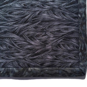 May include: Close-up of a dark gray fabric with a woven pattern of thin lines. The fabric has a dark gray border with a subtle pattern.