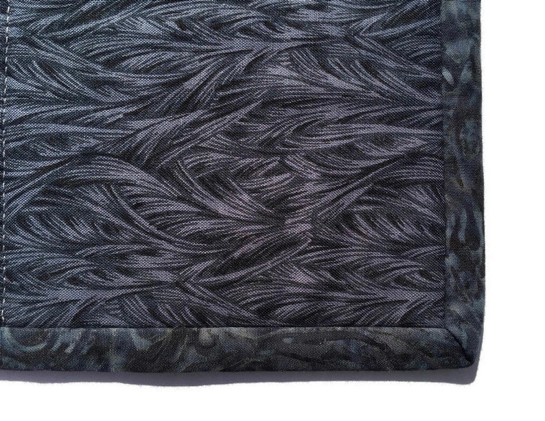 May include: Close-up of a dark gray fabric with a woven pattern of thin lines. The fabric has a dark gray border with a subtle pattern.