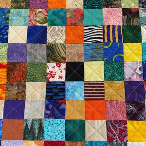 May include: A colourful patchwork quilt featuring a range of fabrics and patterns. The quilt is made up of squares of different colours and designs, including floral, geometric, and abstract patterns. The quilt is stitched together with white thread.