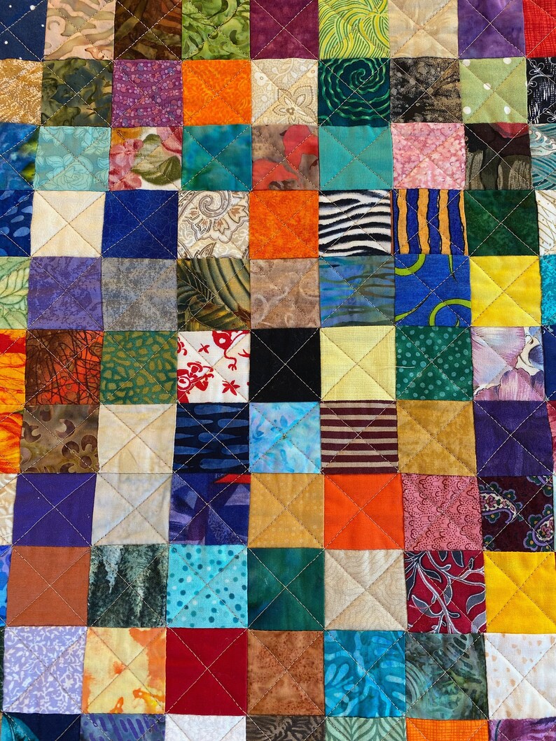 May include: A colourful patchwork quilt featuring a range of fabrics and patterns. The quilt is made up of squares of different colours and designs, including floral, geometric, and abstract patterns. The quilt is stitched together with white thread.