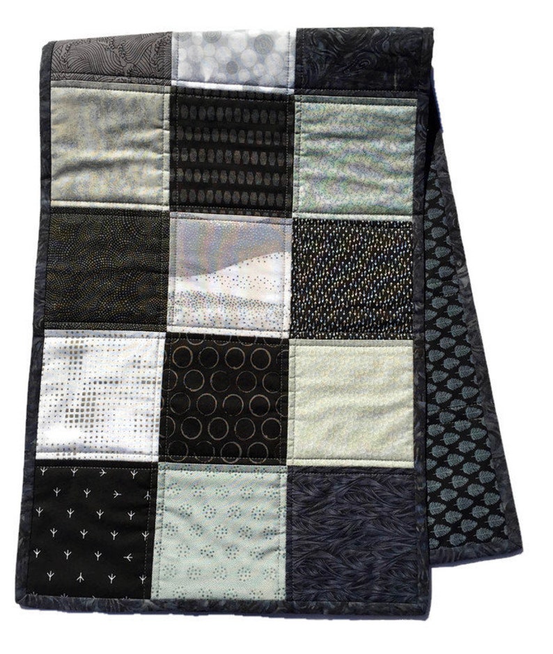 May include: A black and white patchwork quilt with a variety of geometric patterns. The quilt is made of different fabrics with a variety of textures. The quilt is edged with a black fabric.