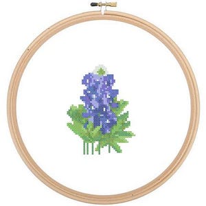May include: A cross-stitch embroidery hoop with a bluebonnet flower design. The flower is purple with green leaves and a white center.