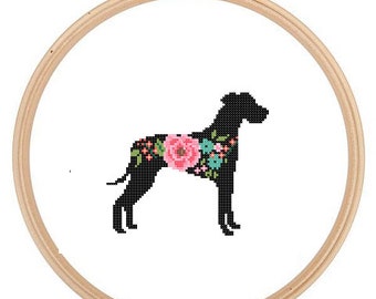 May include: A black silhouette of a dog with floral details in pink, blue, and green. The dog is standing on a white background inside a wooden embroidery hoop.