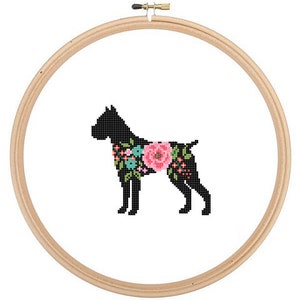 May include: A black silhouette of a dog with floral details in pink, blue, and green. The dog is standing on a white background and is framed in a wooden embroidery hoop.