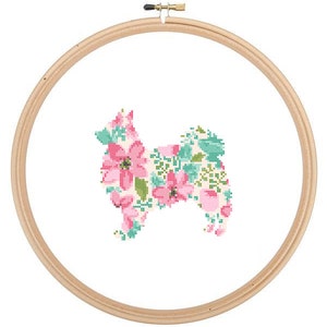 May include: A cross-stitch embroidery hoop with a floral design in the shape of a dog. The flowers are pink, green, and white.