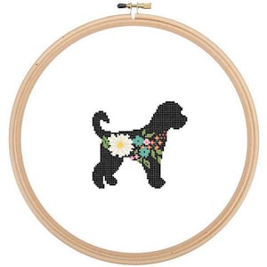 Op de afbeelding: Zwarte silhouet van een hond met een bloemenpatroon op zijn lichaam. De hond staat op een witte achtergrond en is ingelijst in een houten borduurring.